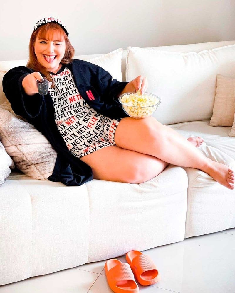 mulher, deitada em um sofá branco, comendo pipoca.