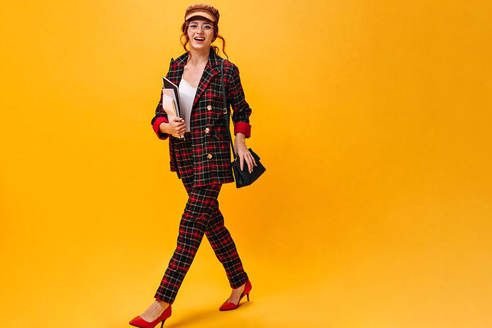 modelo mulher usando um terno com estampas geometricas em cores vermelho vinho e uma camisa preta lisa por baixo em um fundo colorido 