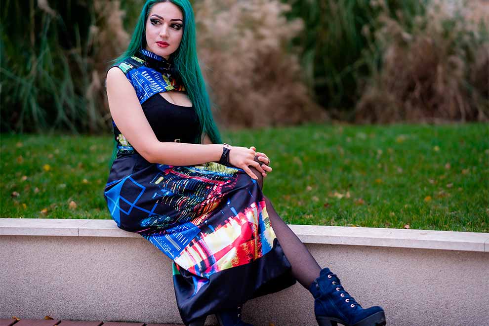 Mulher com cabelo verde e vestido colorido sentada na grama