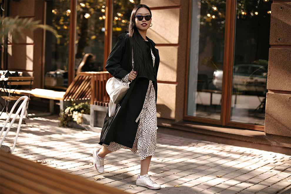mulher usando um vestido midi com bolinhas com um sobretudo preto midi e tênis