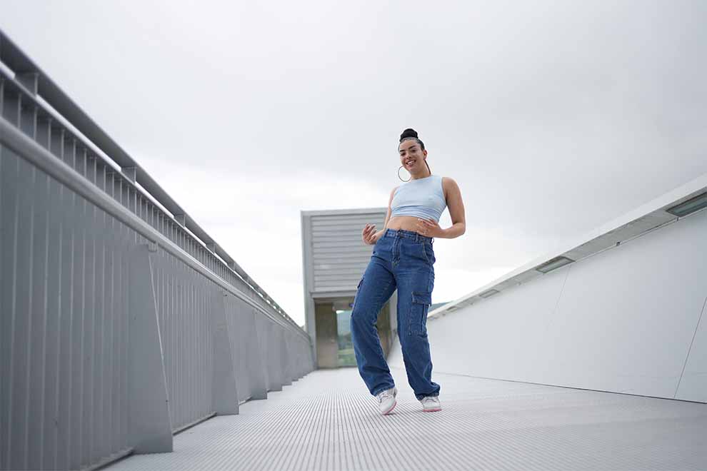 mulher usando calça e regata em cima de uma ponte em um dia nublado