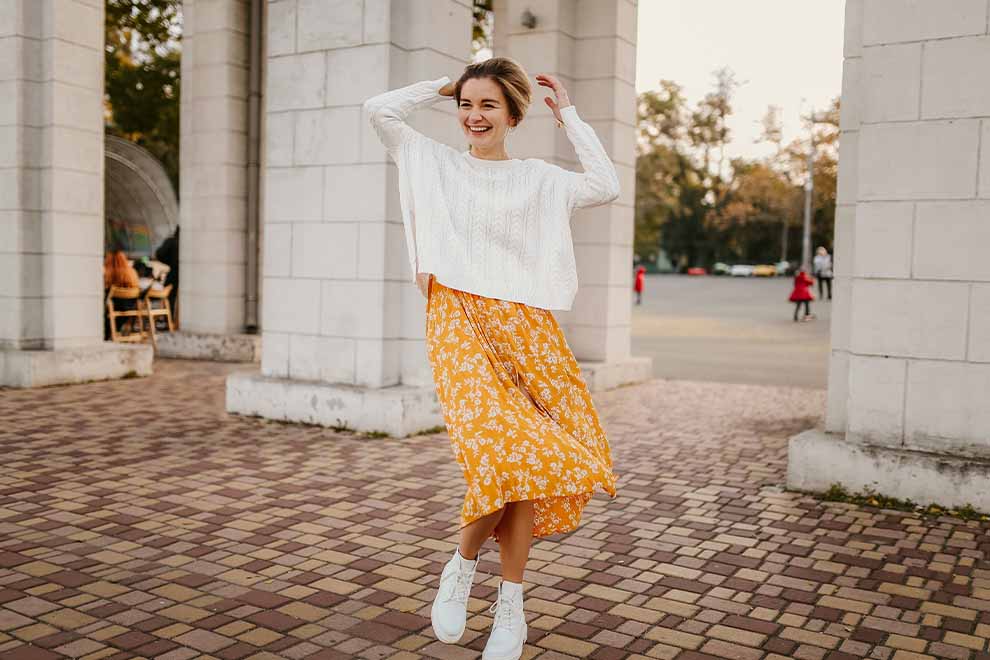 Jovem sorridente com vestido amarelo e suéter branco.