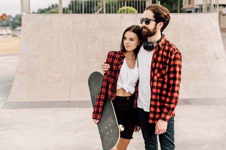 um casal em uma pista de skate com as roupas combinando em xadrez com um skate em baixo dos braços
