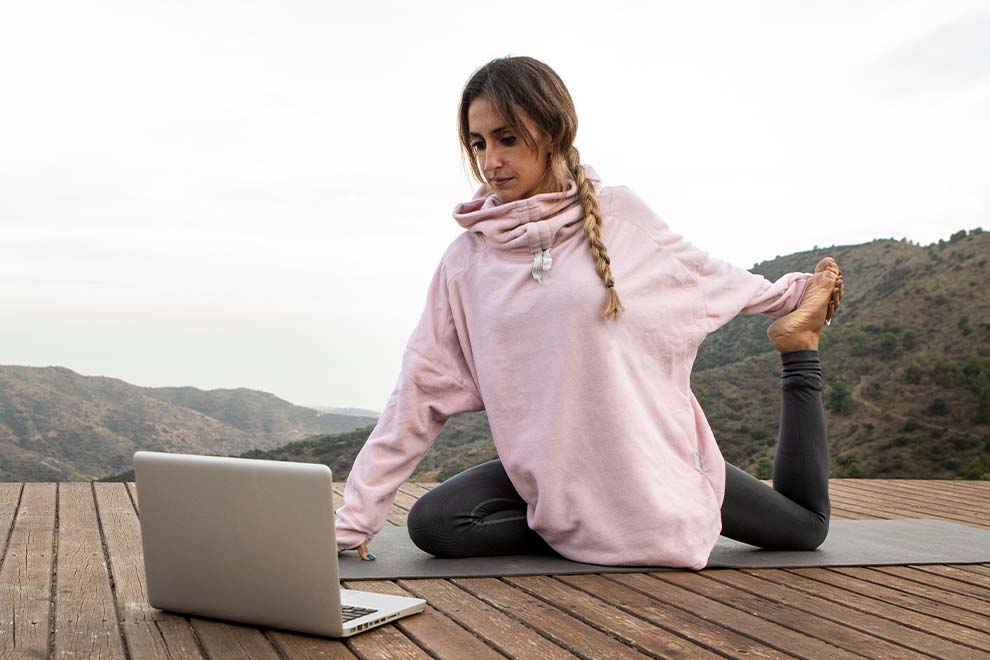 Mulher praticando yoga em frente ao laptop ao ar livre