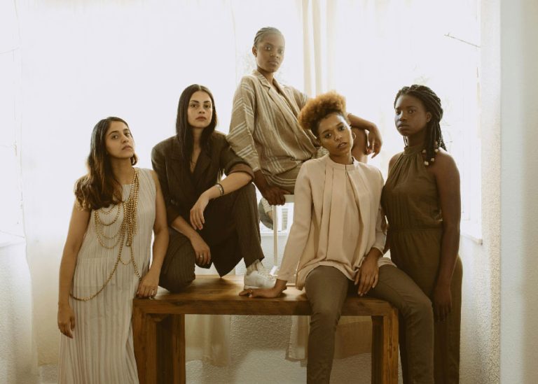 Grupo de mulheres posando com roupas modernas e neutras.