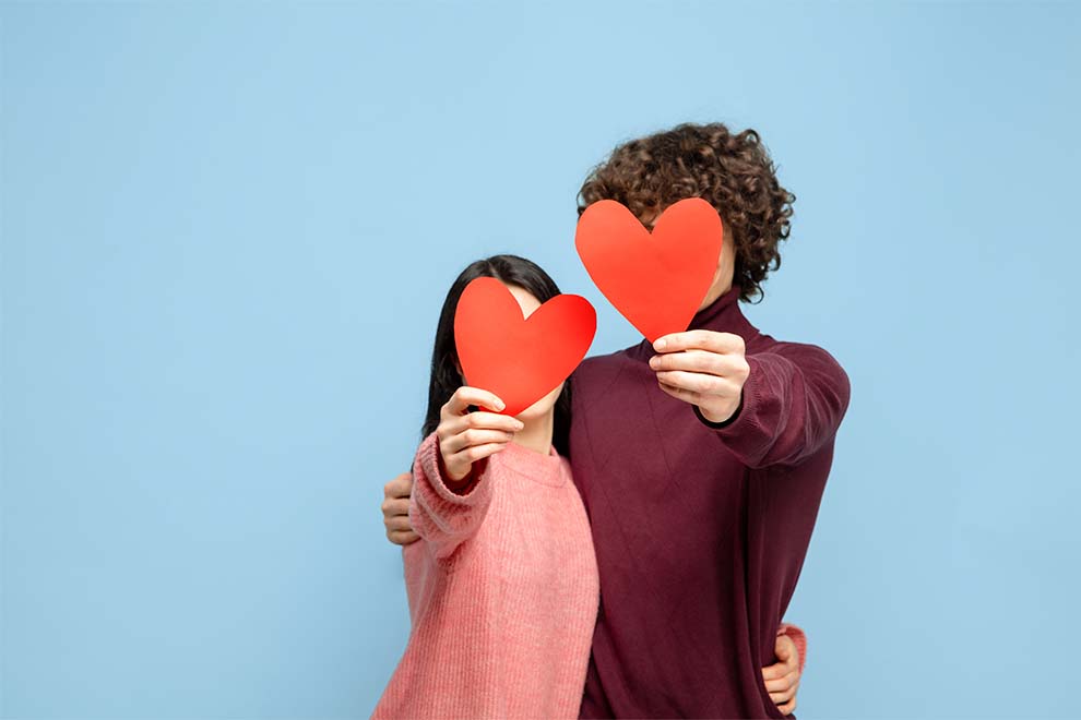 Casal segurando corações vermelhos em fundo azul