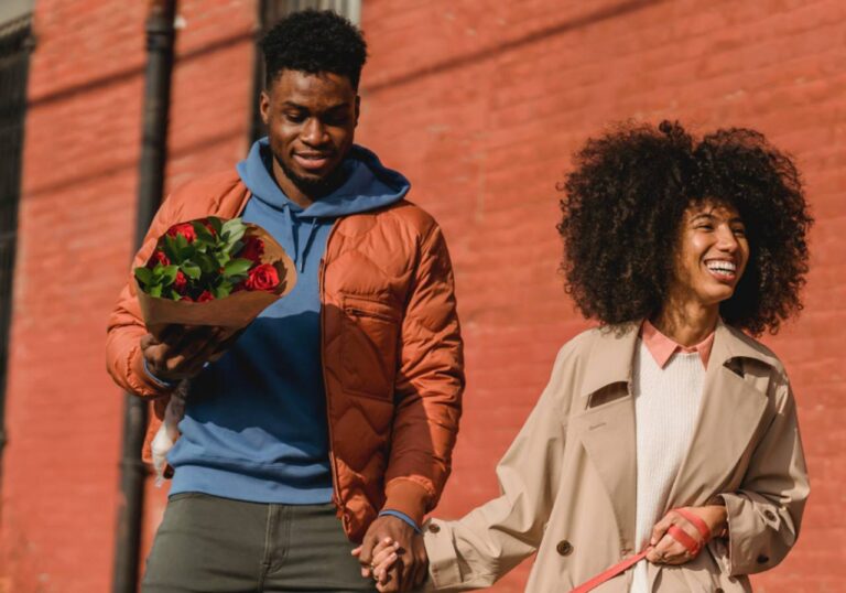 casal jovem andando de mãos dadas sorrindo com buquê de flores