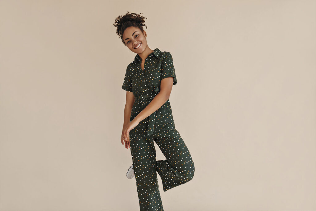 modelo calca estampada verde Imagem de uma modelo feminina, em pé, vestindo um conjunto de roupas confortáveis, com uma calça estampada verde escuro, com tênis, em um fundo bege.